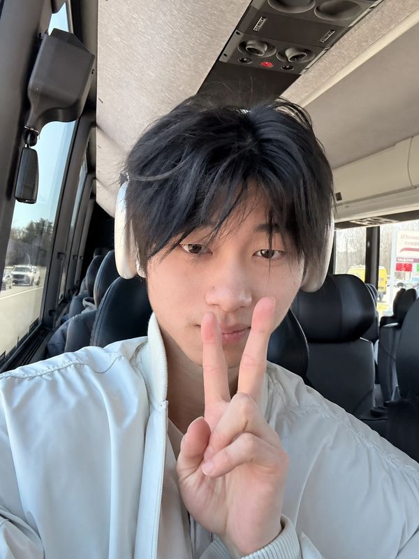 Young man wearing white headphones and jacket giving a peace sign.