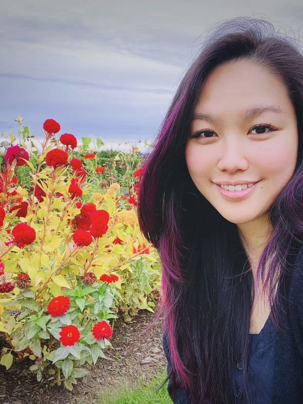 Smiling woman with purple-streaked hair near red flowers.