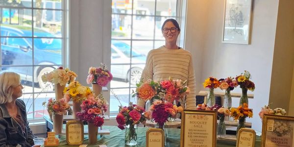 Woman standing behind a table full of colorful flower bouquets for sale.