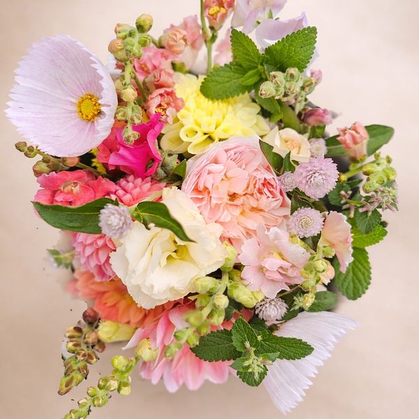 A vibrant bouquet of mixed flowers in soft pink, yellow, and white hues with lush green leaves.