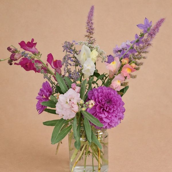 Bouquet of mixed colorful flowers in a glass jar against a beige background.