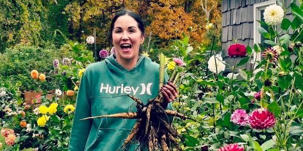 Woman joyfully holding freshly harvested root vegetables in a vibrant garden.