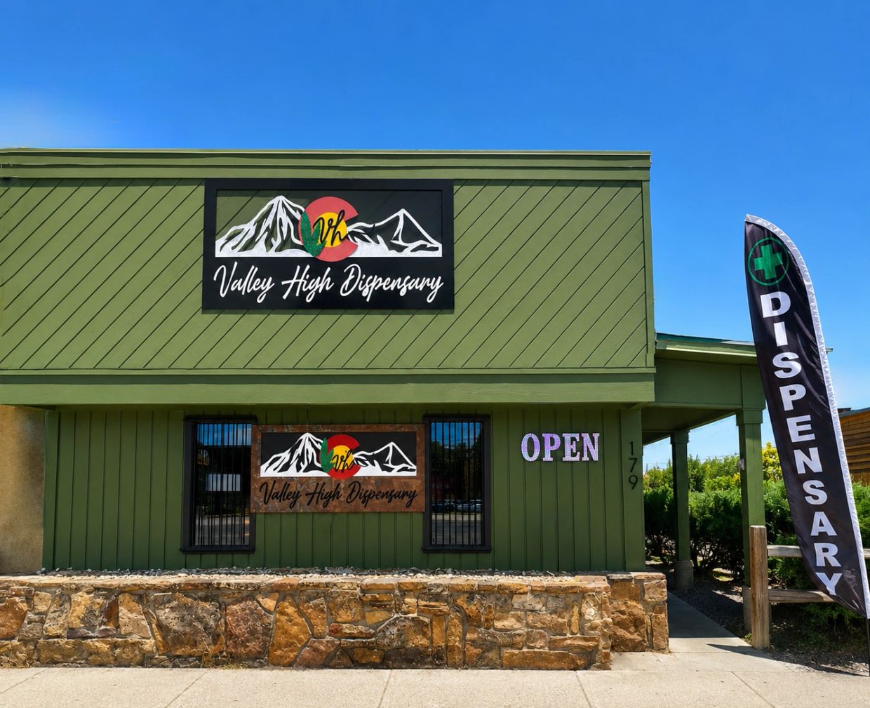 Green dispensary building with signs and a flag.