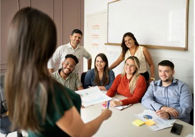A woman presents to a smiling group in a meeting.