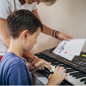 piano teacher pointing to keyboard and holding colored music note flashcard, while boy plays piano
