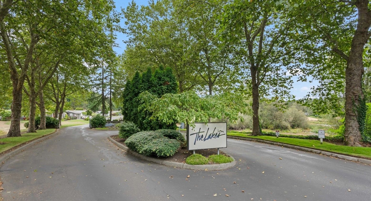 Entrance to a community named The Lakes with lush greenery and a paved road.