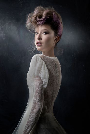 Woman with styled hair and lace dress against a dark background.