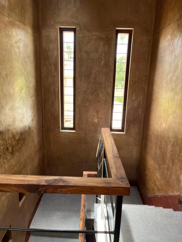Staircase with wooden railing and tall narrow windows in an earthy-toned interior.