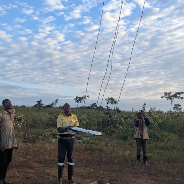 Three men standing in a field holding wires against a cloudy sky.