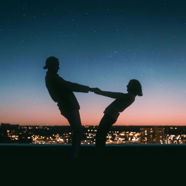 Two people holding hands against a twilight cityscape.