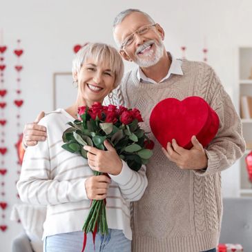 Happy elderly couple celebrating love with roses and heart-shaped gift box.