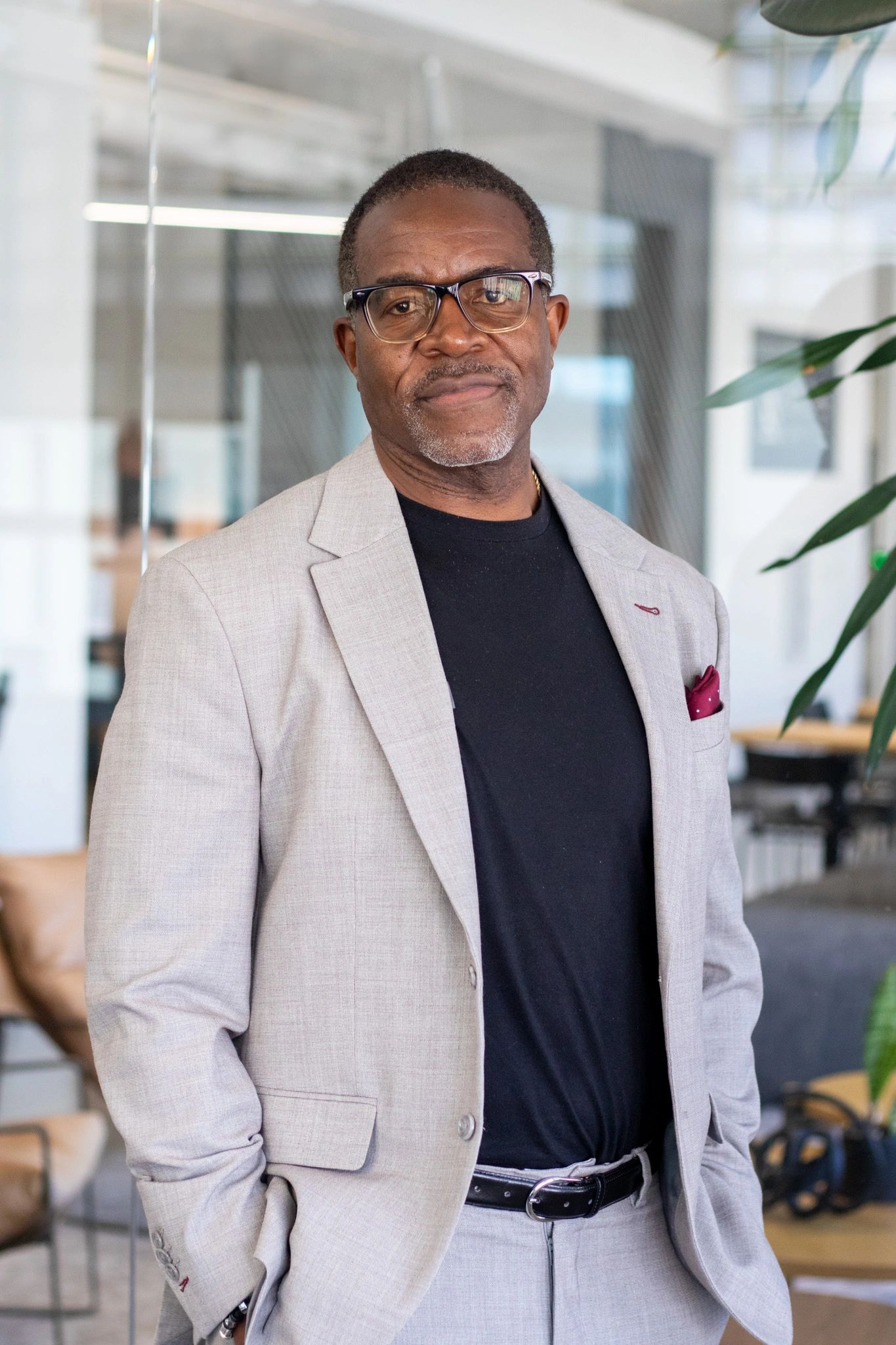 Confident man in beige suit and glasses posing indoors.