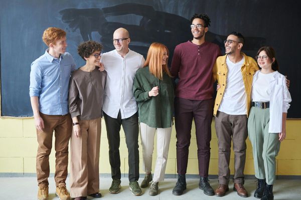 A diverse group of seven young adults standing and smiling together indoors.