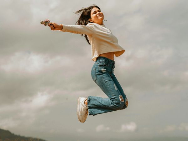 Young woman joyfully jumps in a field under a cloudy sky.