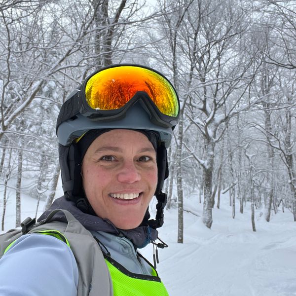 Smiling woman in ski gear on a snowy forest trail.