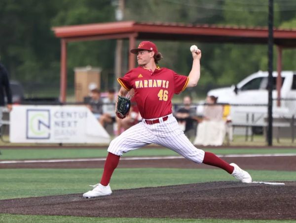 Baseball pitcher in mid-throw wearing a red and yellow uniform on the mound.