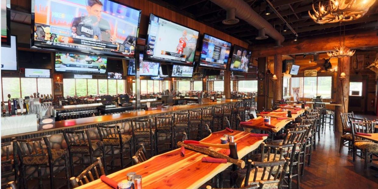 Rustic sports bar with wooden tables, multiple TVs, and antler chandeliers.