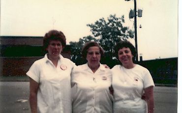 Three women in white uniforms posing outdoors in front of a building.