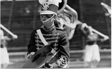 Black and white photo of a marching band member with cymbals.