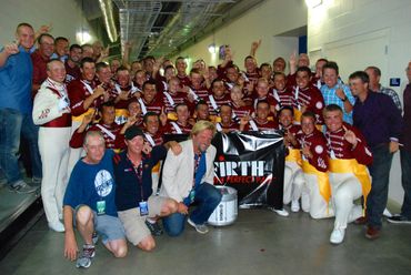 Large group of people celebrating indoors, many in maroon and white uniforms.