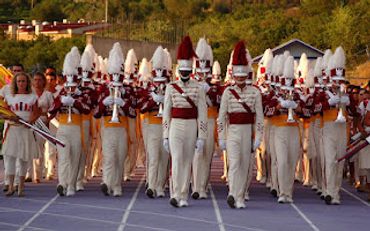 Marching band in uniform performs on a track field.