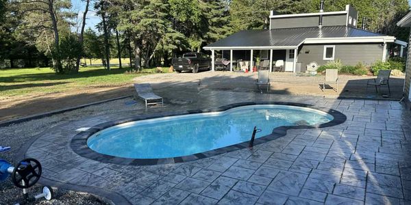 A kidney-shaped pool in a spacious backyard with a modern house.