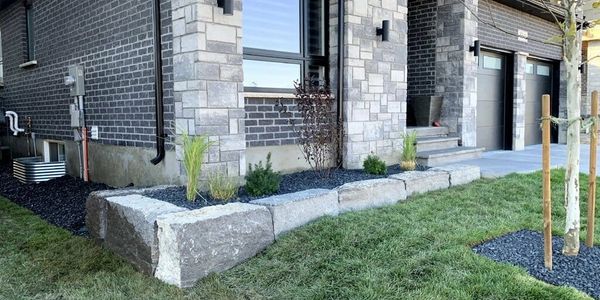 Stone retaining wall and garden bed beside a modern house.