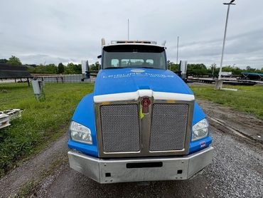Front view of a blue Kenworth semi-truck parked outdoors.