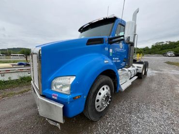 Blue semi-truck parked on gravel with overcast sky.