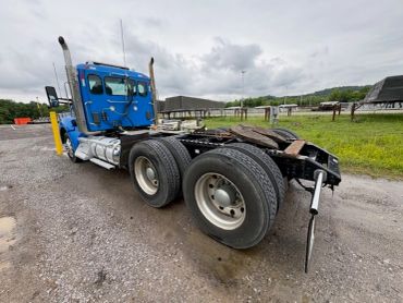 Blue semi-truck tractor parked on gravel with cloudy sky.
