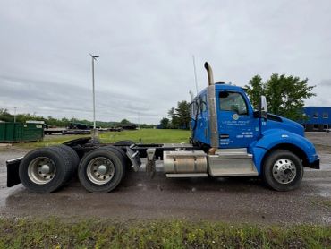 Blue semi-truck cab parked on gravel under cloudy sky.