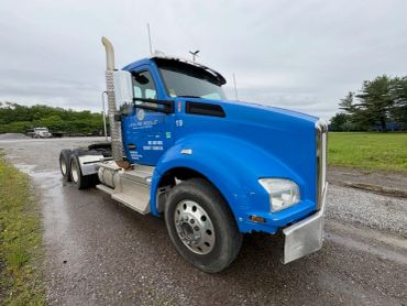 Blue semi-truck parked on a gravel road on a cloudy day.