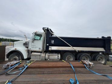 A white and black dump truck parked with metal beams strapped nearby.