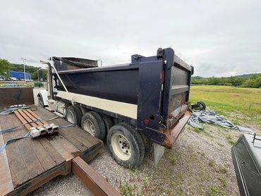 A large dump truck parked on gravel near a flatbed trailer and open field.