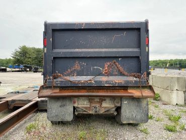 Rear view of an old, rusty dump truck on gravel.