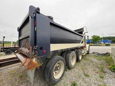 A large black and white dump truck parked on a gravel surface under a cloudy sky.