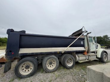 Side view of a large black and white dump truck on gravel.