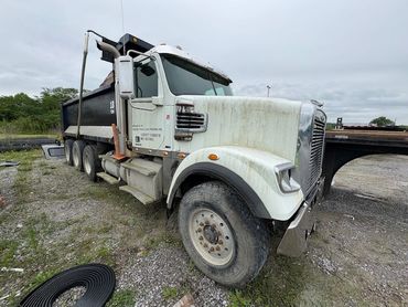 White dump truck parked on gravel under a cloudy sky.
