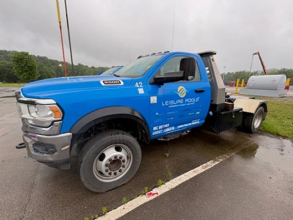 Blue Leisure Pools truck parked on wet pavement on a cloudy day.