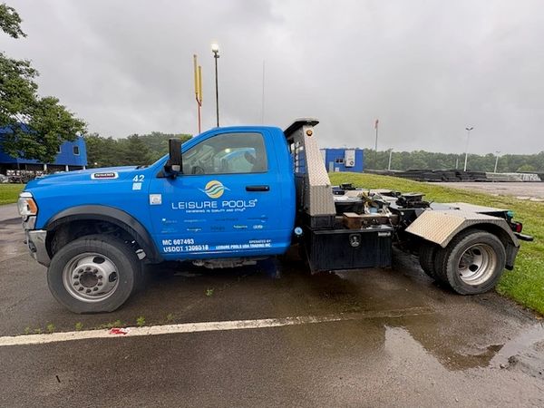 Blue Leisure Pools truck parked on wet pavement under cloudy sky.