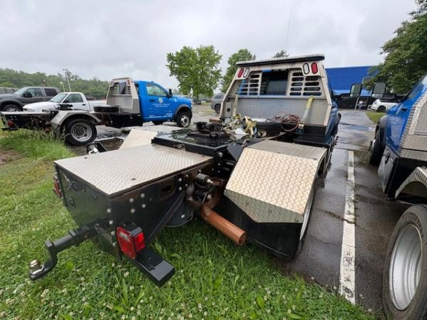 Custom flatbed truck with diamond plate storage compartments and towing hitch.