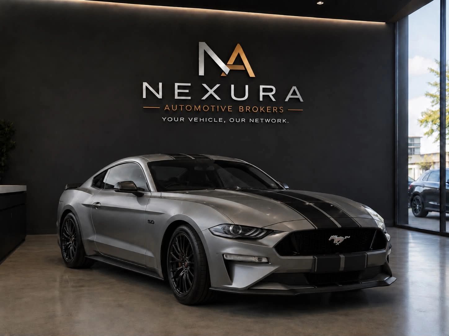 Sleek silver Ford Mustang with black racing stripes inside Nexura Automotive Brokers showroom.