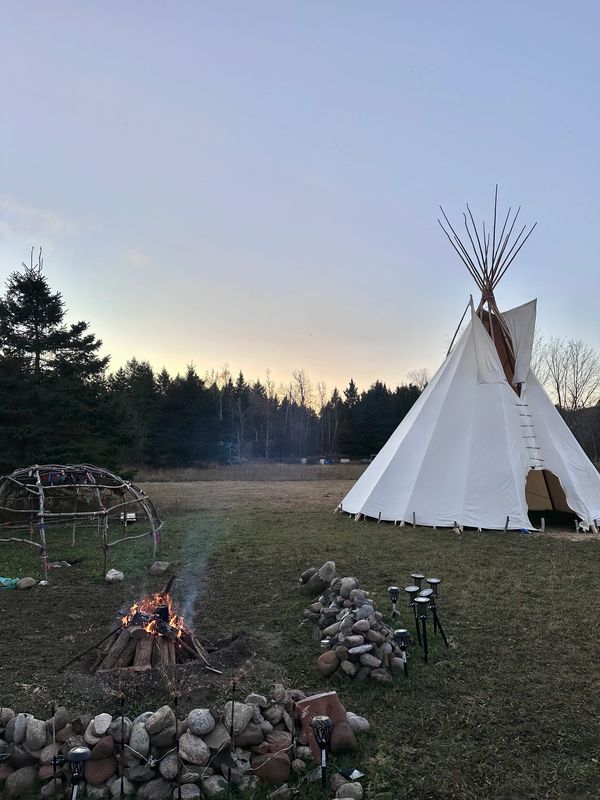 A tipi and campfire set up in a grassy clearing at dusk.