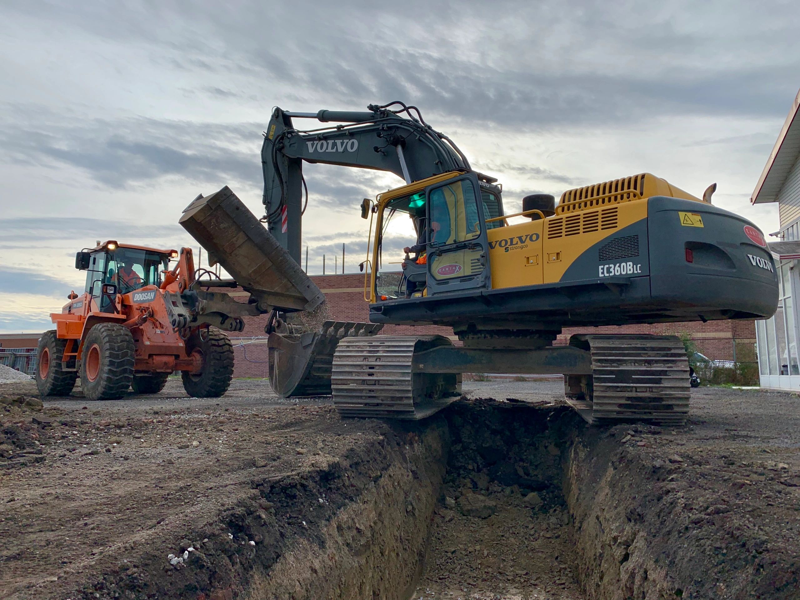 Excavators at work digging a trench on a construction site at dusk.