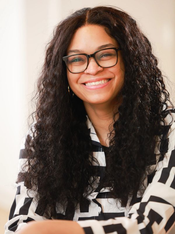 Smiling woman with curly hair and glasses in a striped shirt.