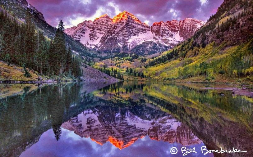 Mountain range reflecting in a lake at sunset with purple clouds. 

