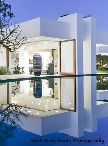 Modern white house with large vase reflected in a calm pool at dusk.
