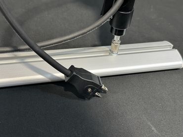 A black power cord and a metallic rail on a dark surface.