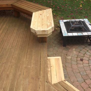 Wooden outdoor bench and a stone fire pit on a patio.