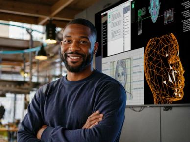A man stands confidently in front of a screen showing 3D facial recognition models.